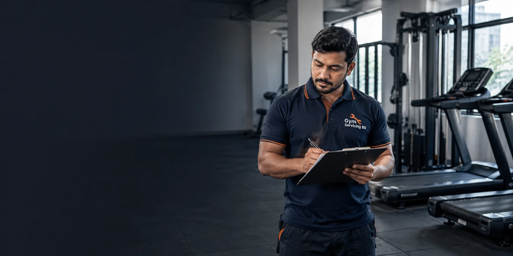 Technician in a navy Gym Servicing BD polo reviewing a gym setup schedule beside treadmills and a cable station.