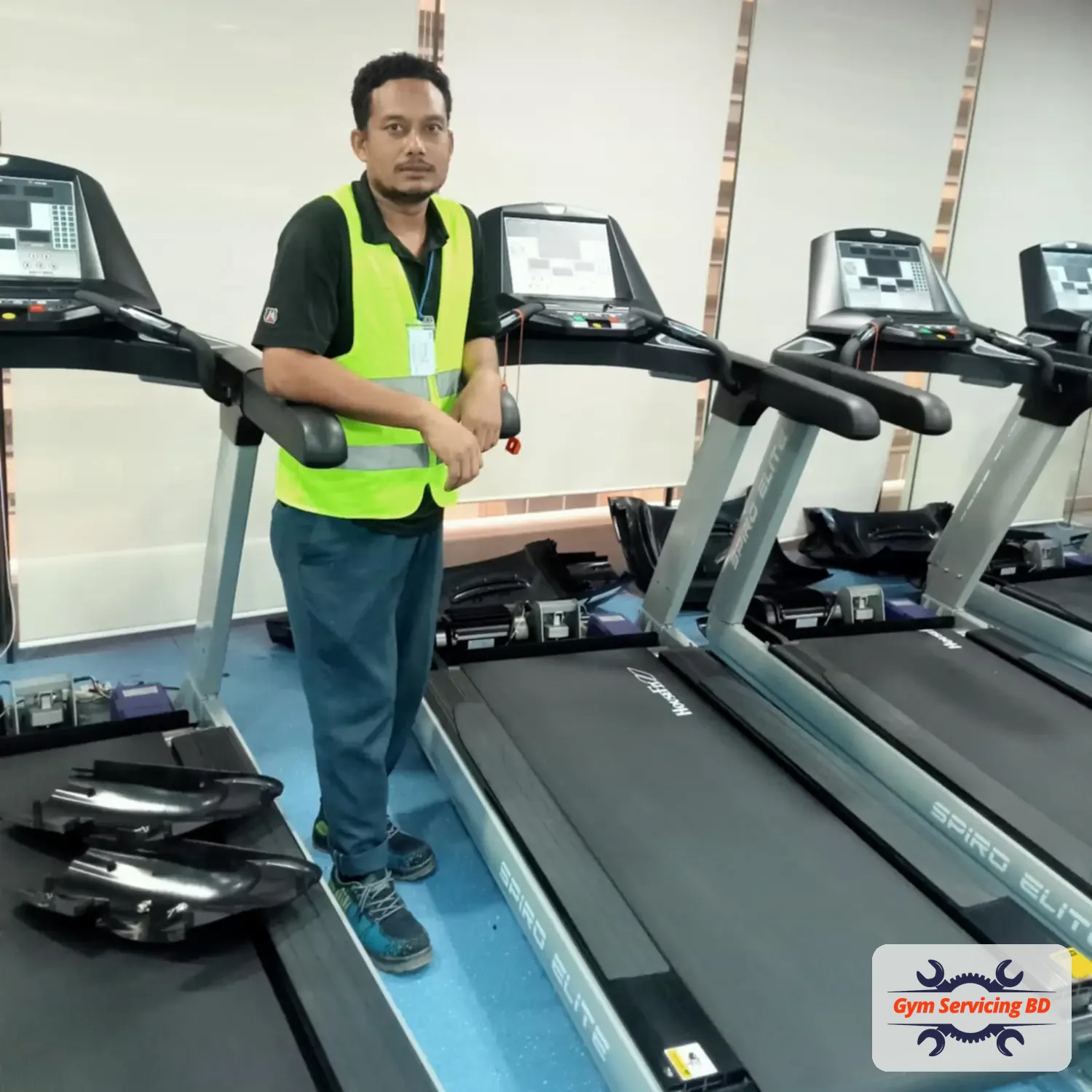 Gym equipment technician beside a row of treadmills in a training room